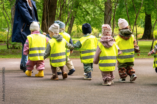 Bild auf Leinwand Kindergarten teacher leading a group of children in yellow safety vests on a wal