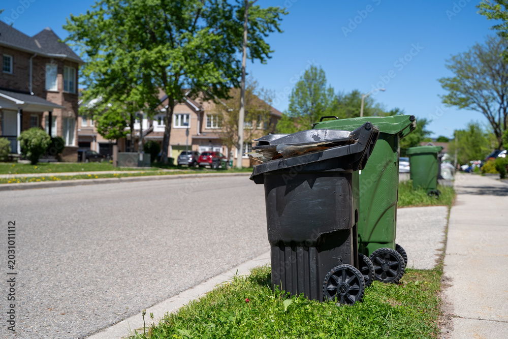 Naklejka premium Black residential garbage bin on suburban street.