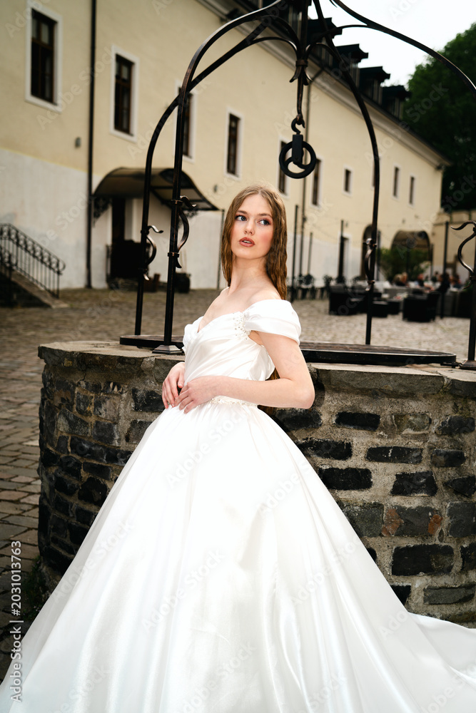 Fototapeta premium Elegant bride in white wedding dress posing in historic courtyard 