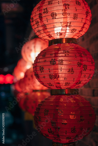 Illuminated traditional red Chinese lanterns adorn a dark brick wall during a vibrant night festival celebration