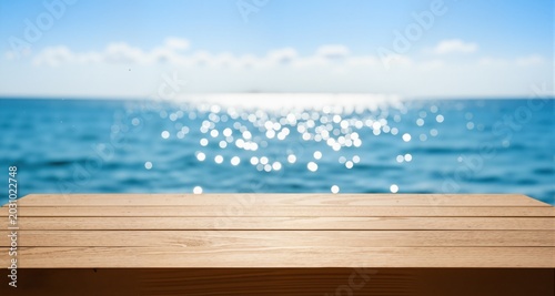 Wood table top on blur sparkling sea water and summer sky background

