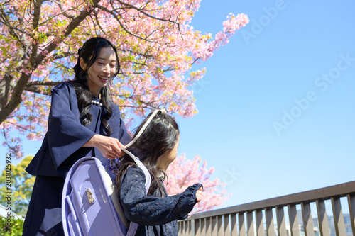 桜の下で子供にランドセルを背負わせる日本人の母親