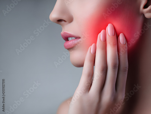 Young woman touching jaw with hand and red pain glow near joint, close up of profile with soft skin and pink nails expressing discomfort