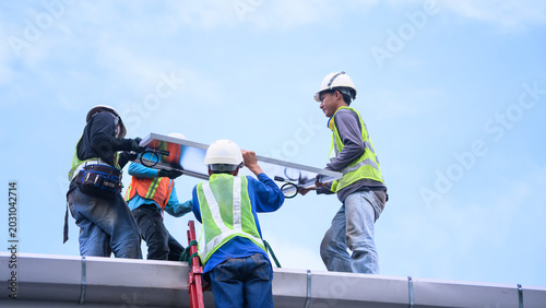 Workers Installing Solar Panel on Rooftop with Safety Gear and Hard Hats Against Blue Sky