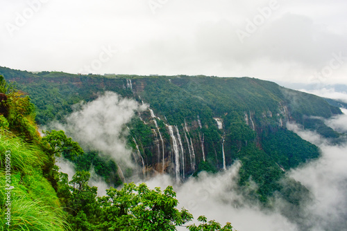 Panoramic landscape of Seven Sisters Falls surrounded by dense greenery and low clouds, revealing the scenic beauty of Meghalaya, India.