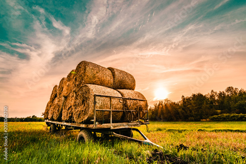 Photos Modern red agricultural tractor hauling a large trailer loaded with round hay ba