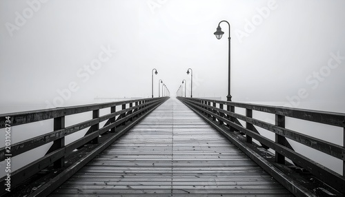 A monochrome pier stretches into thick fog, lined with lamps.  Wooden planks create path