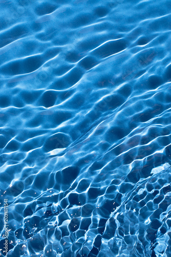 Turquoise textured blue water with waves, abstract summer background. Bright, vibrant color, shiny background.