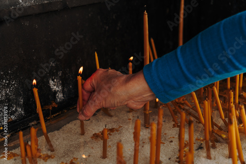 Fotografija Person places a lit candle into white sand inside a religious shrine