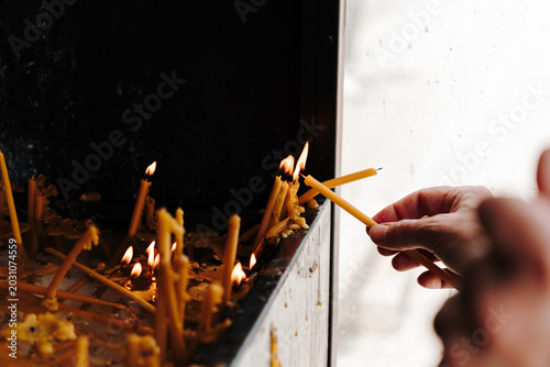 Принти на полотні Human hand places thin candles into a religious prayer stand