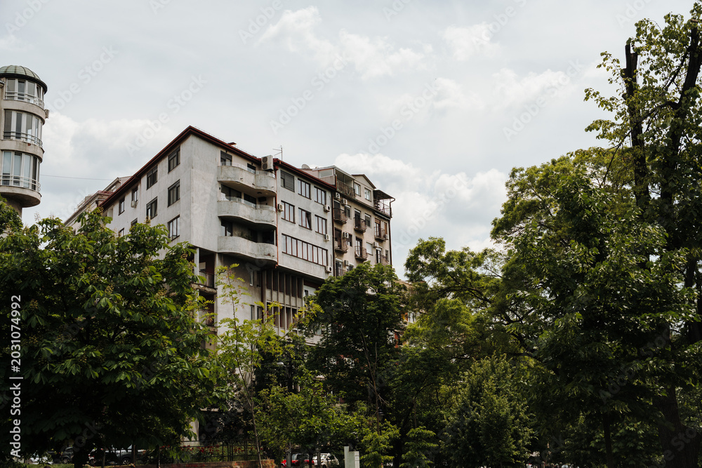 Fototapeta premium Apartment buildings rise above green trees under cloudy sky in Belgrade Serbia. Concept of urban living, residential estate and peaceful city lifestyle