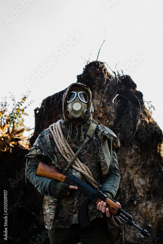 фотографія Post-apocalyptic survivor or stalker in a gas mask and military camouflage holdi