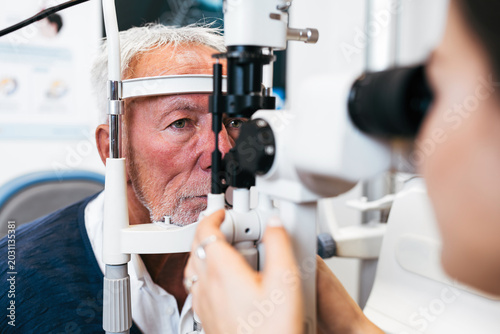 Canvas Print An elderly male patient undergoes a professional eye exam using a slit lamp microscope conducted by a female ophthalmologist in a modern clinic