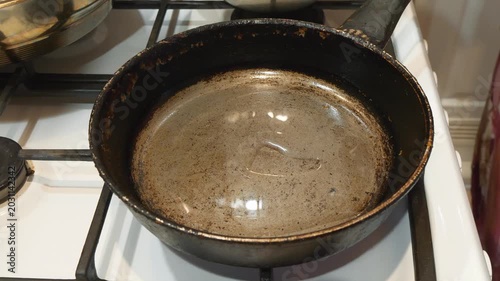 The cook pours a vegetable oil from a glass bottle into a frying pan before frying. Frying pan is on a gas stove