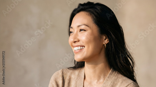 Joyful woman with dark hair laughing looking upward against warm beige textured wall background