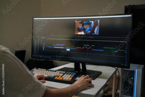Videographer monitoring widescreen display, adjusting video timeline and audio tracks in post-production studio, crafting seamless visual narrative for digital media, close-up, cropped shot.