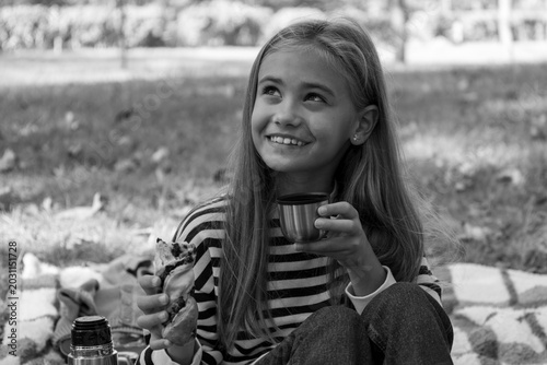 Slika na platnu Black and white candid portrait of a smiling young girl enjoying a picnic outdoors in a natural park setting