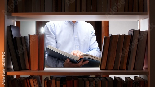 Schilderij op canvas Man reaching for and holding an open book, reading from a bookshelf with many vo