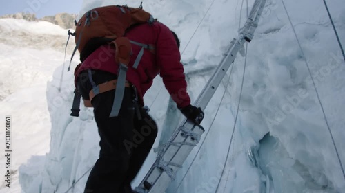 Determined female mountaineer carefully crossing a dangerous glacial crevasse on a fixed ladder