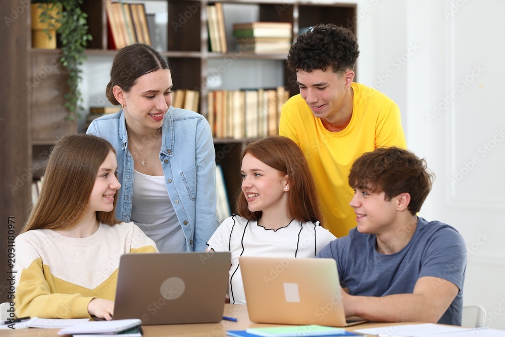 Fototapeta premium Group of students studying with laptops and notebooks at wooden desk in classroom