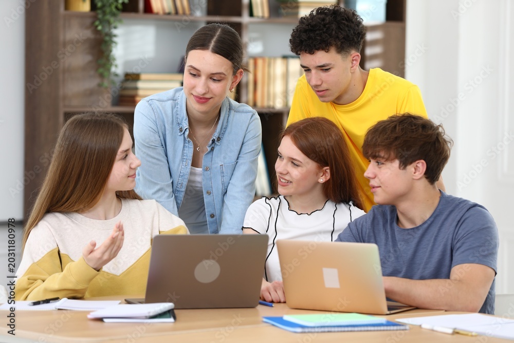Fototapeta premium Group of students studying with laptops and notebooks at wooden desk in classroom