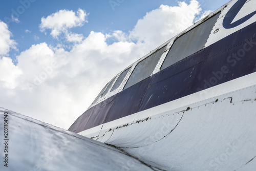 Картината върху платно Close-up of a weathered vintage aircraft fuselage and cockpit section displayed at an aviation museum, showing aged metal surfaces, markings, and historic aviation engineering under a blue sky