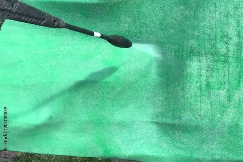 Person cleaning a green carpet with a powerful pressure washer, ideal for cleaning service advertisements, DIY cleaning guides, or product demonstrations