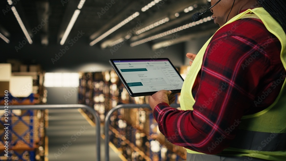 Fototapeta premium Female employee assisting clients with package tracking and delivery status, verifying AWB and shipment tags on tablet. Managing customer service complaints on headset, distribution hub.