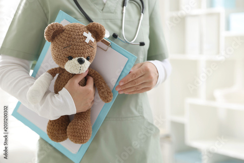 Fotografie Pediatrician holding teddy bear with adhesive bandages in clinic, closeup