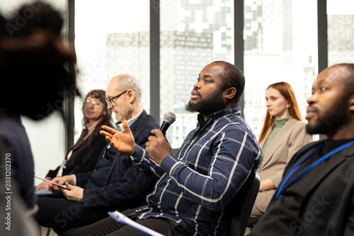 Fotografie African american person in attendance asking questions on microphone to engage in debate at business conference, professional people sharing opinion, interacting in panel discussion