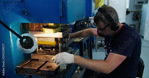Punch press operator operating stamping machine with protective gear, industrial metal fabrication process