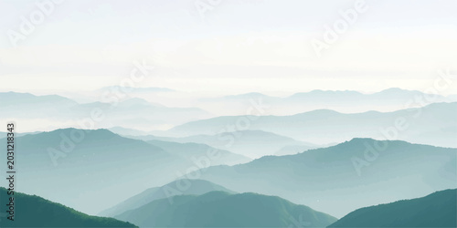 A beautiful morning mist and low clouds roll through the blue valley at sunrise, framing a dramatic mountain landscape with a silhouette of trees along the foggy hills