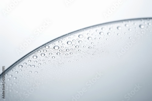 Glass surface with water droplets on curved edge and soft pale background