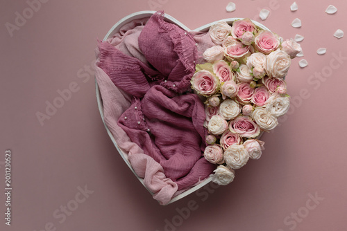 A heart-shaped box decorated with pink roses and fabric on a pink background. A newborn photo session basket.