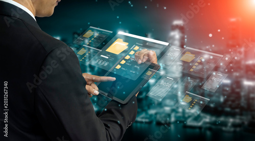 Obraz na plátně A business professional interacts with a tablet displaying virtual files in a modern urban setting at night, showcasing innovative technology and digital workspace solutions