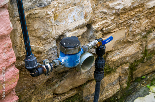 Cuadro en lienzo Outdoor water meter with pipes and valve on stone wall