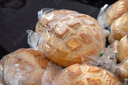 A display of artisan breads in clear plastic bags for sale at a farmer's market. The crusty, sourdough, pumpernickel, white, whole wheat, and traditional homemade rustic loaves are on display for sale