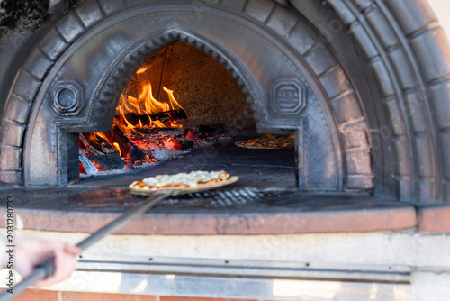Fotografie Artisan pizza being placed blazing wood-fired oven