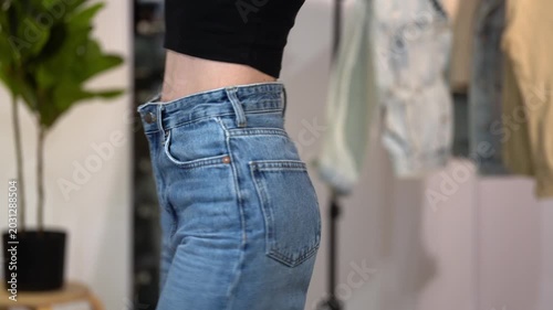 Slender woman turns in high waist blue jeans, showing front, side and back fit in home interior. Concept of flattering denim silhouette, body confidence, fashion styling and wardrobe appeal