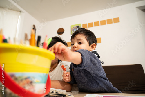 Foto Little Mexican boy reaching for colored pencils in a yellow bucket at home