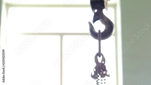 Crane beam with hook and cable hanging in front of large window in huge factory. metallurgical production, metal processing, heavy industry manufacturing process. construction site . 4 k video