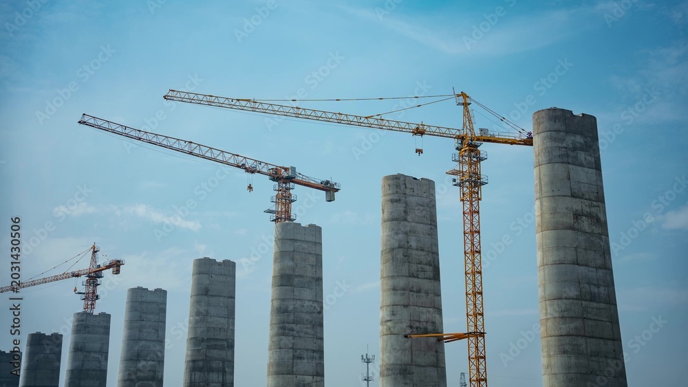 Fototapeta premium Tower cranes and piers at construction site under blue sky