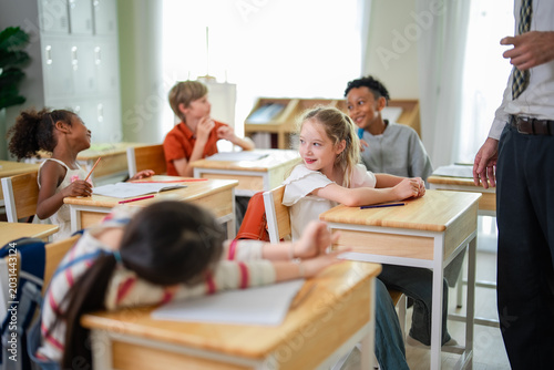 Multicultural elementary school children smiling and interacting during classroom activity while teacher supervises in bright educational environment.