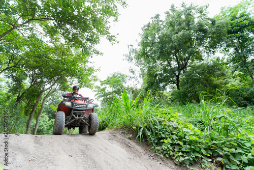 Foto Person rides ATV through tropical path in sunny weather with green plants and ta