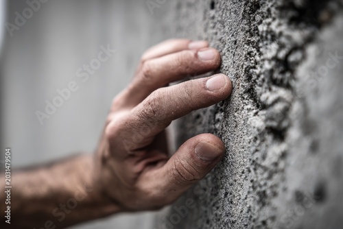 Close-up of a male hand touching a textured concrete wall