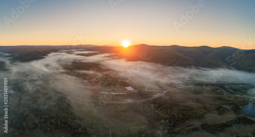 Fotografija Sunrise mist settling over a tranquil rural valley, revealing a winding river an