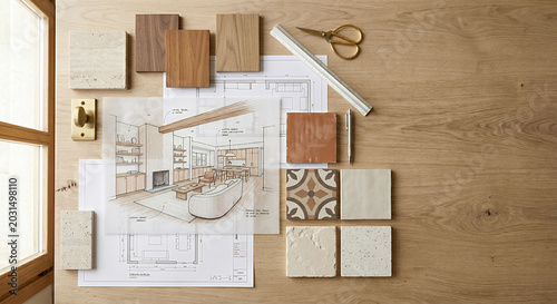 Interior design materials and sketches are laid out on a wooden surface, including wood samples, tiles, blueprints, and a brass door handle. 