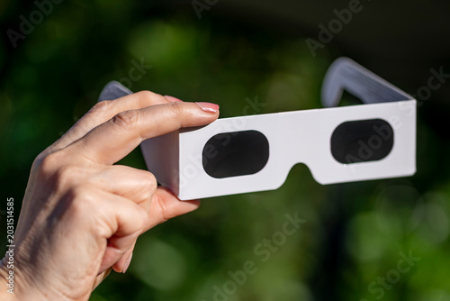 A female hand holds a pair of special glasses for observing the sun, against a dark green background