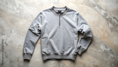 Casual gray pullover sweatshirt with a quarter zip neck and front pockets laid flat on a mottled stone surface for fashion advertising