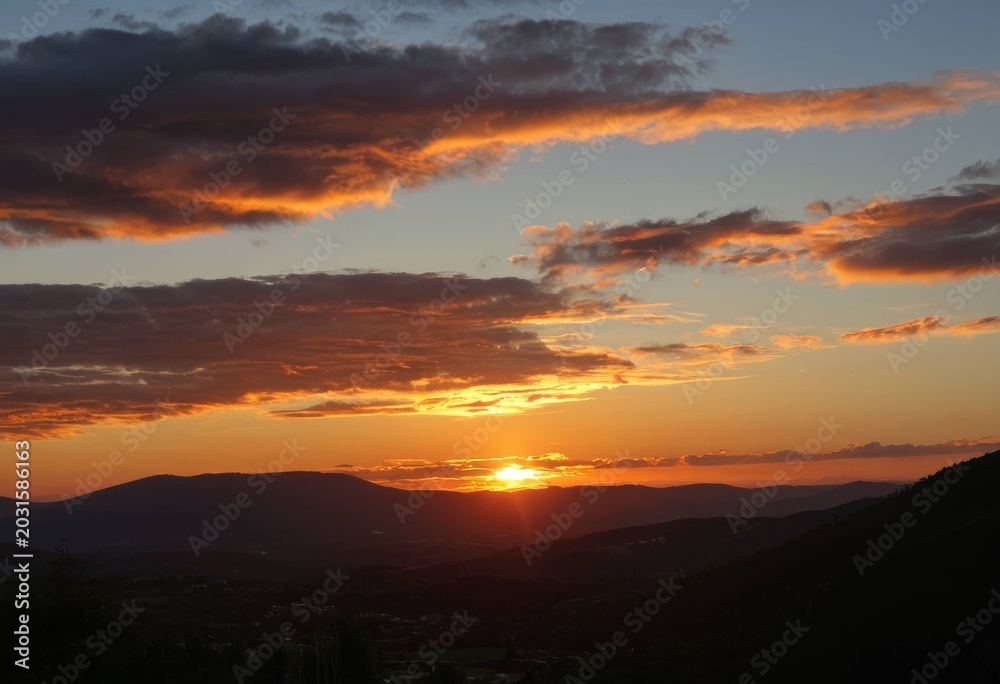Fototapeta premium Vibrant Orange Sunset and Dramatic Clouds Setting Behind Mountain Range